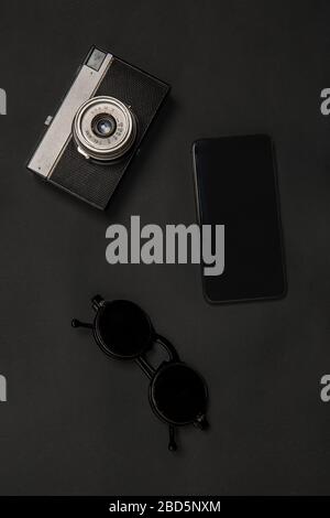 Gadgets and eyewear. Monochrome stylish and trendy composition in black color on studio background. Top view, flat lay. Pure beauty of usual things around. Copyspace for ad. Retro camera, smartphone. Stock Photo