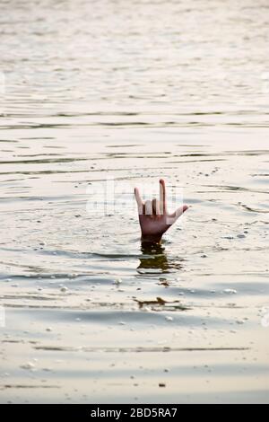 Human hand raised on wave water surface. Help wanted sign of finger wanting a helping hand. Stock Photo