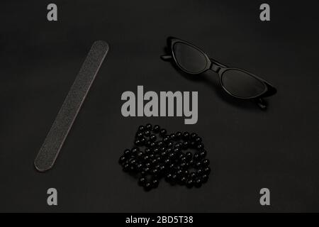 Fashion look. Nailfile, eyewear, chain. Monochrome stylish and trendy composition in black color on studio background. Top view, flat lay. Pure beauty of usual things around. Copyspace for ad. Close up. Stock Photo
