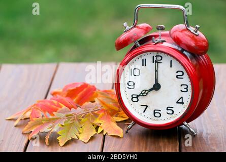 Red alarm clock with orange autumn leaves on a wooden background, daylight savings time concept Stock Photo