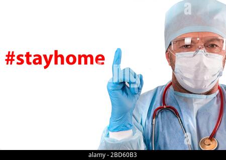 Doctor in a medical gown, hat, glasses and gloves warns #stayathome during the coronavirus epidemic. The doctor in personal protection raised his inde Stock Photo