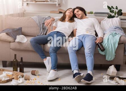 After party. Young couple sleeping drunk on couch in messy room Stock Photo