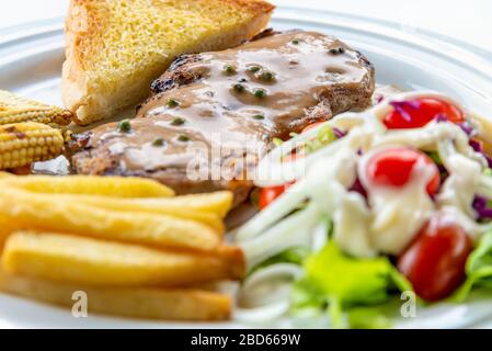 Closeup side view steak pork chop with creamy pepper sauce, Served with french fries, toast, grill baby corn, roast carrot, and vegetables salad on a Stock Photo