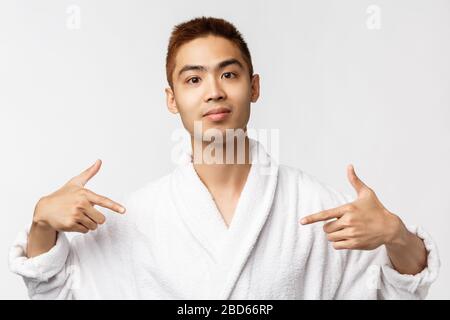 Beauty, spa and leisure concept. Portrait of confident, upbeat smiling asian man in bathrobe, pointing fingers at himself like pro, bragging, being Stock Photo