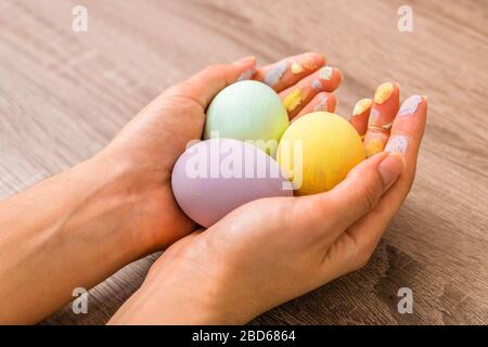 easter concept. closeup beautiful woman hands holding three eggs colored in tender pastel colors yellow, mint and purple over wooden table Stock Photo