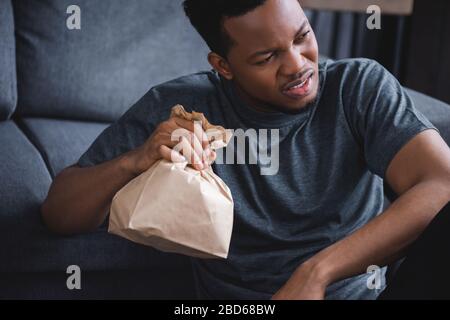 Worried african american man holding paper bag while having panic attack at home Stock Photo