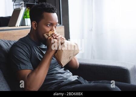 stressed african american man breathing with paper bag while having panic attack at home Stock Photo