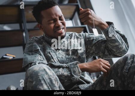 crying african american soldier holding army badge at home, suffering from PTSD Stock Photo