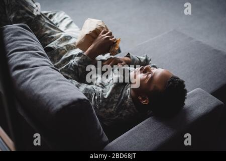 african american soldier in military uniform holding paper bag while having panic attack and suffering from PTSD at home Stock Photo