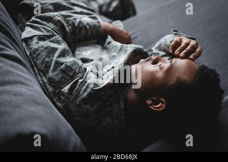 tired african american soldier in military uniform sleeping in sofa at home Stock Photo