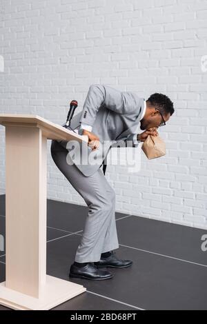 stressed african american speaker breathing with paper bag and having panic attack on business conference Stock Photo