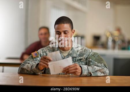 US Army soldier smiles happily as he opens his letters from home. Stock Photo