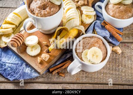 Portioned Banana bread mugcake in small mugs. Easy sweet baking idea, With fresh bananas, nuts, honey and spices on rustic wooden background copy spac Stock Photo