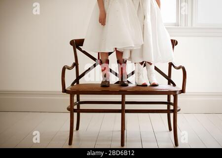 Two girls standing on a chair while dressed up in party clothes and cowboy boots. Stock Photo
