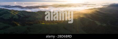 A beautiful sunrise illuminates fog as it rolls through valleys in Northern California. Just west of these hills and valleys is San Francisco Bay. Stock Photo