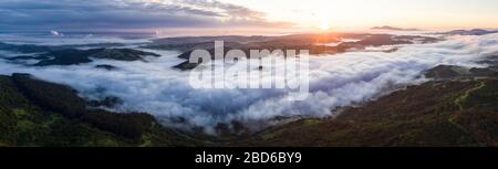 A beautiful sunrise illuminates fog as it rolls through valleys in Northern California. Just west of these hills and valleys is San Francisco Bay. Stock Photo