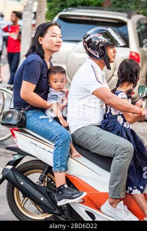 A family cling on to each other on a small moped as they make their way through the busy streets of Phnom Penh. Stock Photo