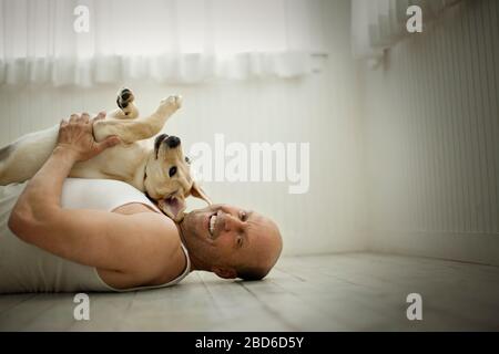 Middle aged man lying on the floor and holding his Labrador dog. Stock Photo