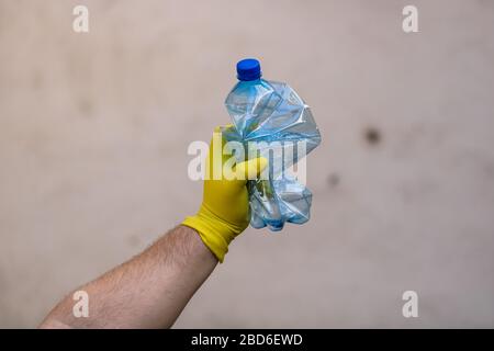 Hand with rubber glove holding smashed empty plastic bottle isolated on a blurred background. Recycle and volunteer concept. Environmental pollution a Stock Photo