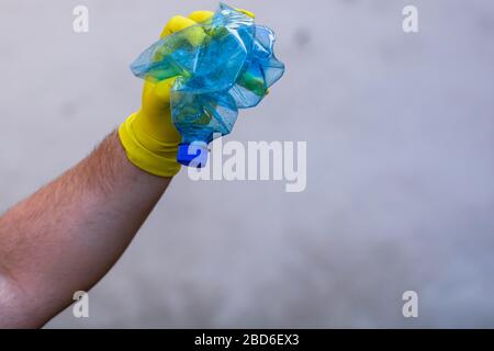 Hand with rubber glove holding smashed empty plastic bottle isolated on a blurred background. Recycle and volunteer concept. Environmental pollution a Stock Photo