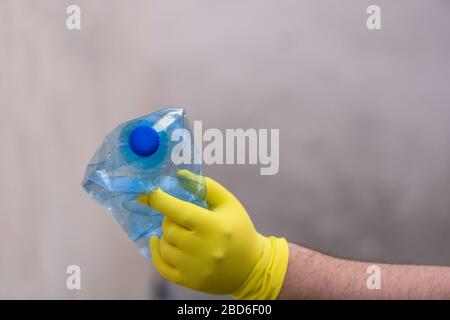 Hand with rubber glove holding smashed empty plastic bottle isolated on a blurred background. Recycle and volunteer concept. Environmental pollution a Stock Photo