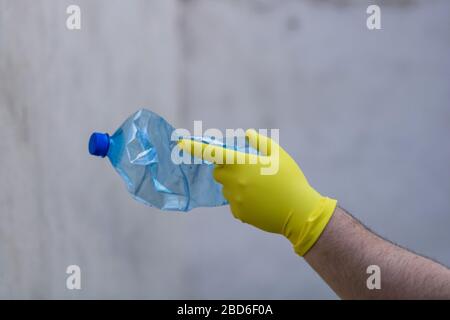 Hand with rubber glove holding smashed empty plastic bottle isolated on a blurred background. Recycle and volunteer concept. Environmental pollution a Stock Photo