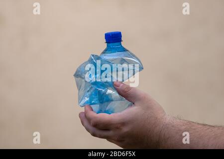 Hand holding smashed empty plastic bottle isolated on a blurred background. Recycle and volunteer concept. Environmental pollution and worldwide ecolo Stock Photo