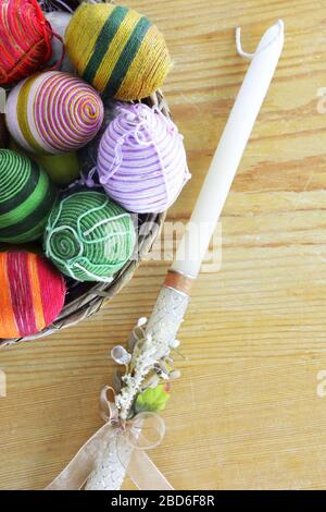 Eggs decorated with threads an Easter candle beside on wooden  table Stock Photo