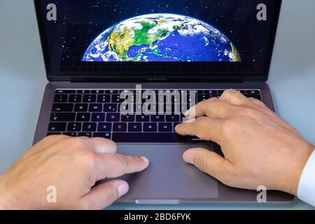 Rome, Italy - April 1, 2020: a man types on the keyboard of an Apple laptop, Macbook pro series. The image of the planet Earth seen from space appears Stock Photo