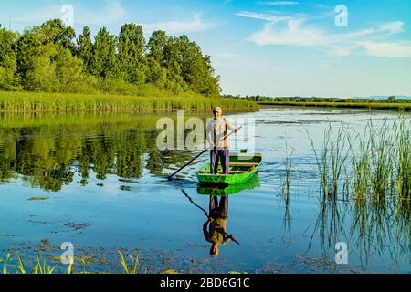 A Serbian man pushing a traditional raft or boat on the river Zasavica, Zasavica national nature park, Serbia, Europe. May 2017. Stock Photo