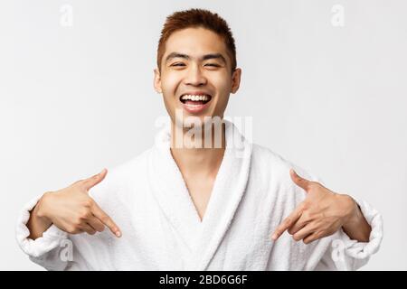 Beauty, spa and leisure concept. Portrait of satisfied pleased, happy asian man in bathrobe pointing at himself and smiling broadly, talking own Stock Photo