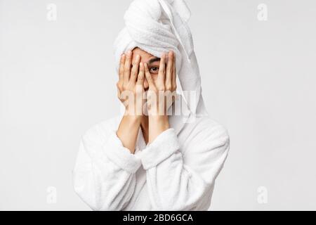Beauty, spa and leisure concept. Funny asian man in bathrobe and bath towel over head, coming from shower, hiding face behind hands and peeking with Stock Photo
