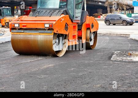 A heavy orange vibratory skating rink compacts hot asphalt on the construction of a new road city street , image with copy space. Stock Photo