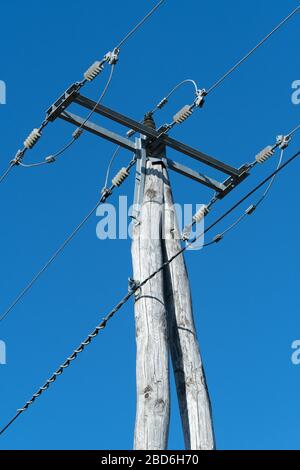 Old wooden three-phase electric utility pole with high voltage electricity cables and a clear blue sky in background. Electricity, power distribution Stock Photo