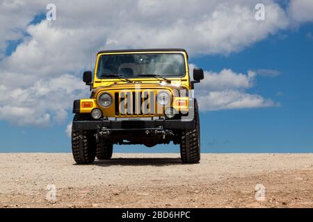 Shoshone National Forest, Wyoming, USA - July 13, 2014:  A gold Jeep Rubicon in a dirt parking area with the dynamic blue sky and white fluffy clouds