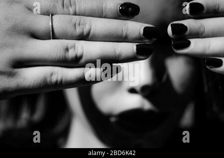Young woman hiding her eyes with the hands. Not wanting to see or not wanting to be seen. Focus on the hands, black and white. Stock Photo