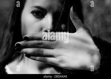 Young woman hiding her mouth with one hand. No freedom of speech, silence. Focus on the hand. Stock Photo