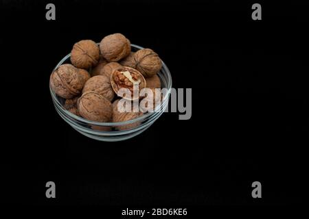 Glass bowl with walnuts in peel on a black background. Copy space.