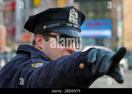 NYPD police officer with sunglasses and peaked cap pointing direction with his leather glove covered hand in Manhattan, New York City, United States Stock Photo