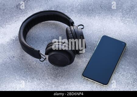 Black headphones and mobile phone on gray background. Social isolation concept. Blank screen of smartphone Stock Photo