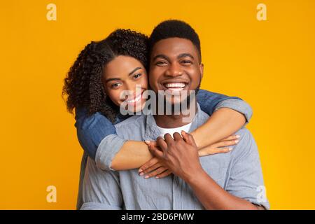 Portrait of joyful millennial woman hugging her boyfriend from behind ...
