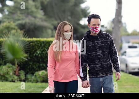 A young couple walking in the neighborhood wearing fabric face masks. Covering face in public is recommended by CDC in many countries during to Covid Stock Photo