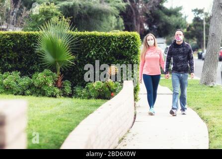 A young couple walking in the neighborhood wearing fabric face masks. Covering face in public is recommended by CDC in many countries during to Covid Stock Photo