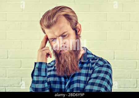 Thinking. Portrait of a worried man casual blue shirt man looking down wards isolated white brick wall background. Yellow Toned image, horizontal. Neg Stock Photo