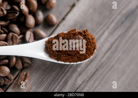 white ceramic spoon with ground coffee on a wooden background Fried Arabica grains. Stock Photo