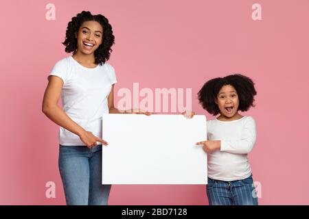 Excited Afro mother and daughter holding and pointing at white placard Stock Photo