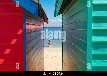 Melbourne Australia - March 11 2020; View between colourful Brighton Beach boxes to water's edge with two people walking along. Stock Photo