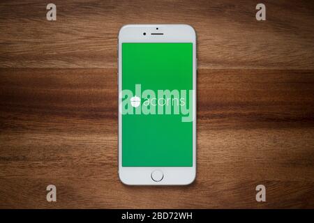 An iPhone showing the Acorns company logo rests on a plain wooden table (Editorial use only). Stock Photo