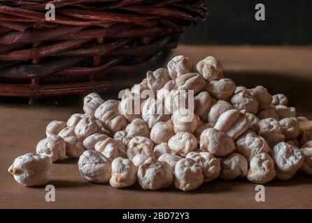 Bunch of raw chickpeas on a wooden table in low key light with a rustic basket in the background, as part of dark food photography Stock Photo