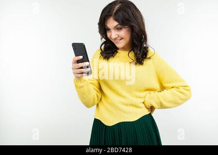 lovely girl in a yellow blouse smilingly peeks at a message on the phone on a white background Stock Photo